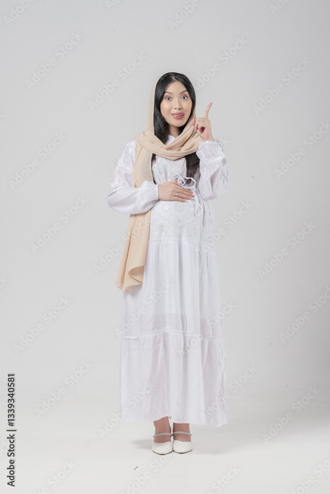 Asian Muslim pregnant woman pointing to the copy space upwards with sticking out tongue expression. Asian Muslim pregnant woman pointing to the copy space upwards with sticking out tongue expression.