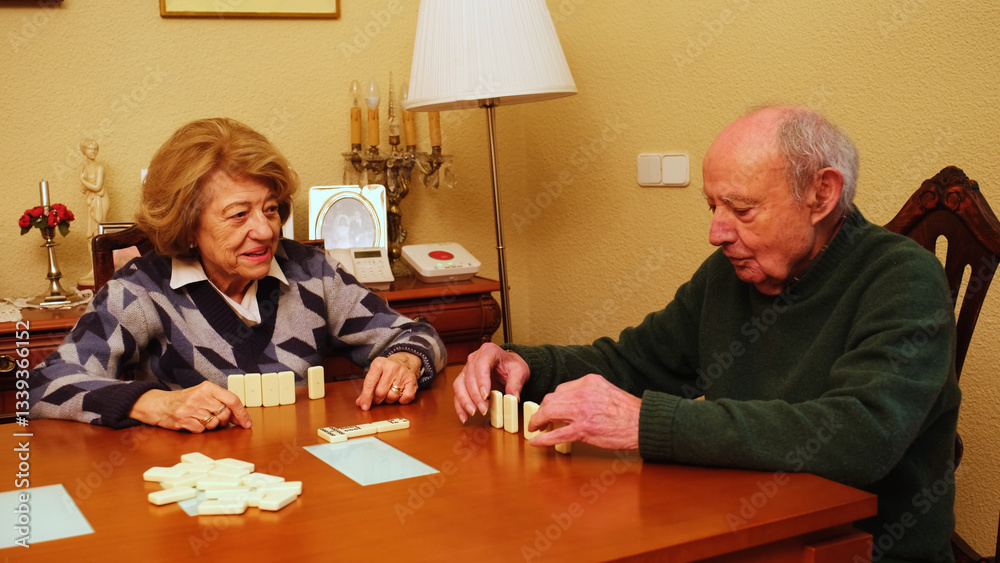 Elderly couple playing dominoes on a wooden table in their living room, enjoying their free time together