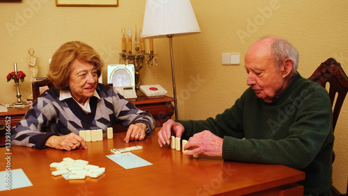 Obraz na płótnie Elderly couple playing dominoes on a wooden table in their living room, enjoying their free time together w salonie