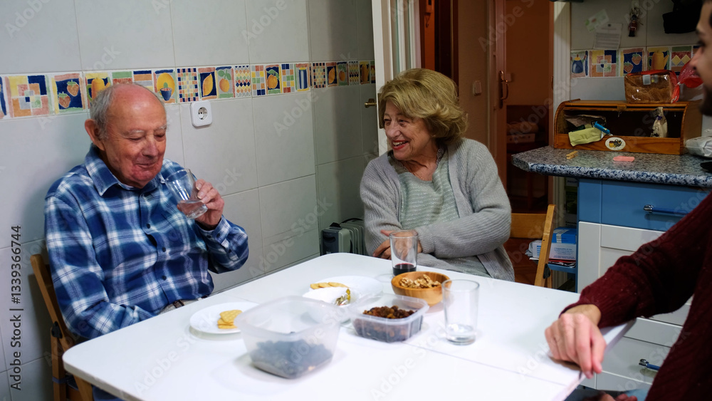 Happy senior man drinking water and talking to wife and family during lunch in kitchen