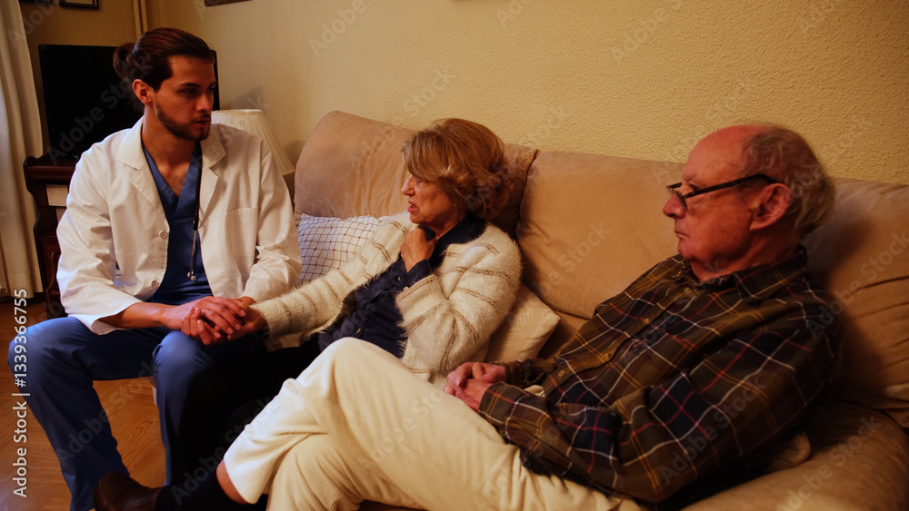 Young male doctor holding hand of senior woman and comforting worried senior couple at home