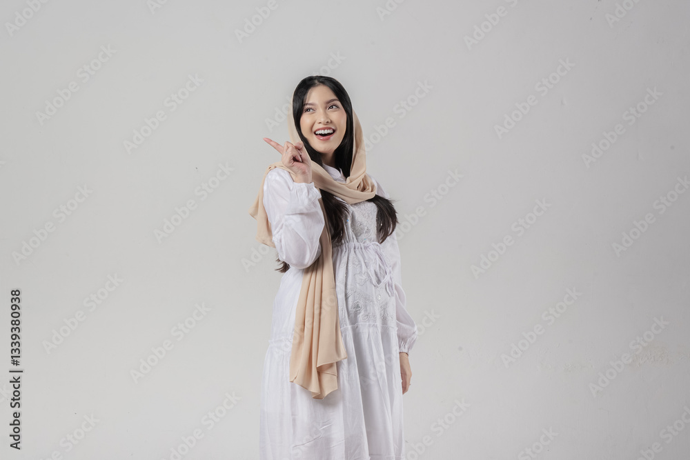 Beautiful Asian Muslim pregnant woman in hijab pointing to the copy space behind her. Beautiful Asian Muslim pregnant woman in hijab pointing to the copy space behind her.