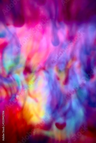 Abstract blur focus vibrant colors flowing with colored inks dispersed in water. The composition consists of shades of blue, red, green and yellow blending and swirling on a light background, creating