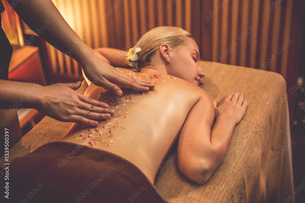 Fototapeta premium Woman customer having exfoliation treatment in luxury spa salon with warmth candle light ambient. Salt scrub beauty treatment in Health spa body scrub. Quiescent