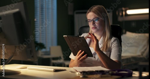 A dedicated healthcare professional is actively using a tablet while in a dimly lit hospital room setting.