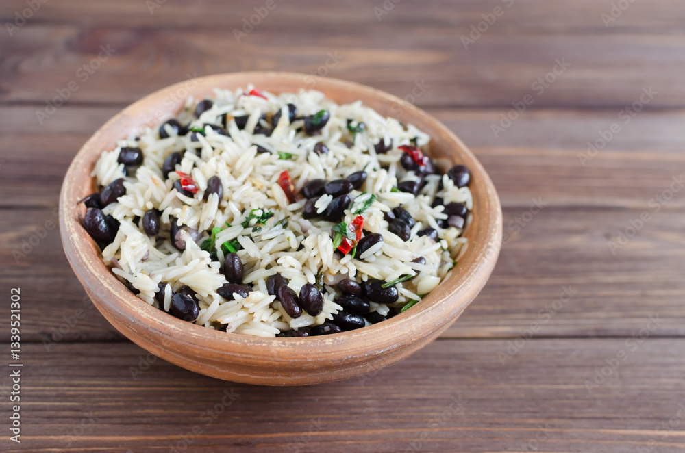 Traditional Costa Rican dish - Gallopinto. Black beans and rice stewed with onions, garlic, cilantro and red pepper in a ceramic bowl on a wooden table. Selective focus. Horizontal orientation Traditional Costa Rican dish - Gallopinto. Black beans and rice stewed with onions, garlic, cilantro and red pepper in a ceramic bowl on a wooden table. Selective focus. Horizontal orientation