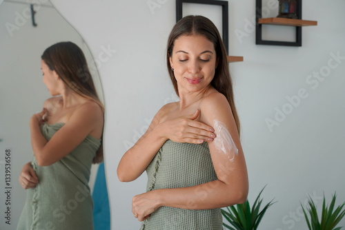 Relaxed pretty woman spreads body cream on arm and takes care of her skin at home
