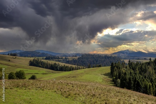 Obraz na płótnie Dramatic clouds gather over rolling hills and lush forests before sunset in a tranquil landscape w salonie