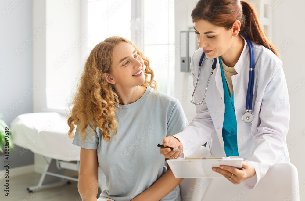 Fototapeta premium Happy smiling young woman patient talking with friendly female doctor therapist holding report file with appointment sitting in office during medical exam in clinic. Medicine and health care concept