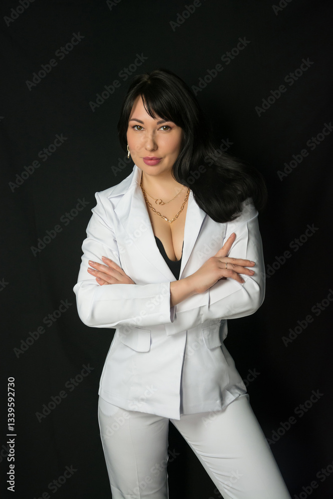 Young brunette woman in a business white suit stands at a black background