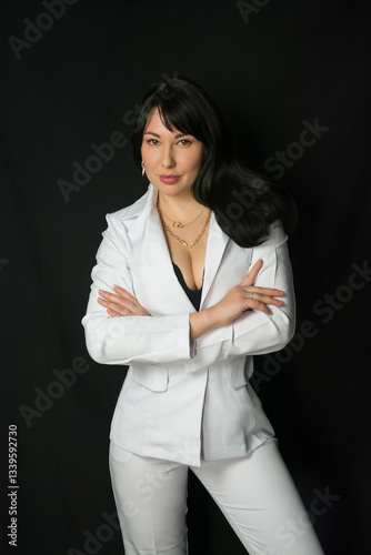 Obraz na płótnie Young brunette woman in a business white suit stands at a black background w salonie