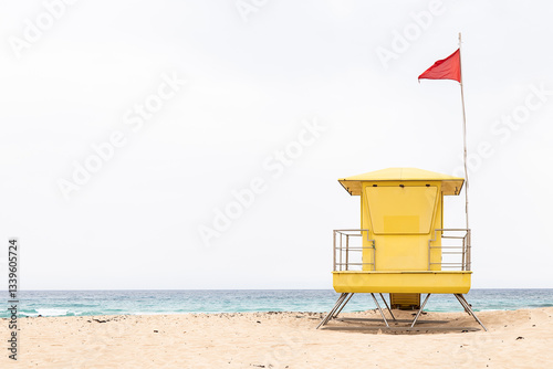 Bright yellow lifeguard tower on sandy beach with red flag