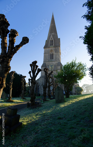 Christ church in Swindon, UK. Tree avenue towards entrance at sunrise in the winter. Dormant tree sculptures. Vertical view from a graveyard.