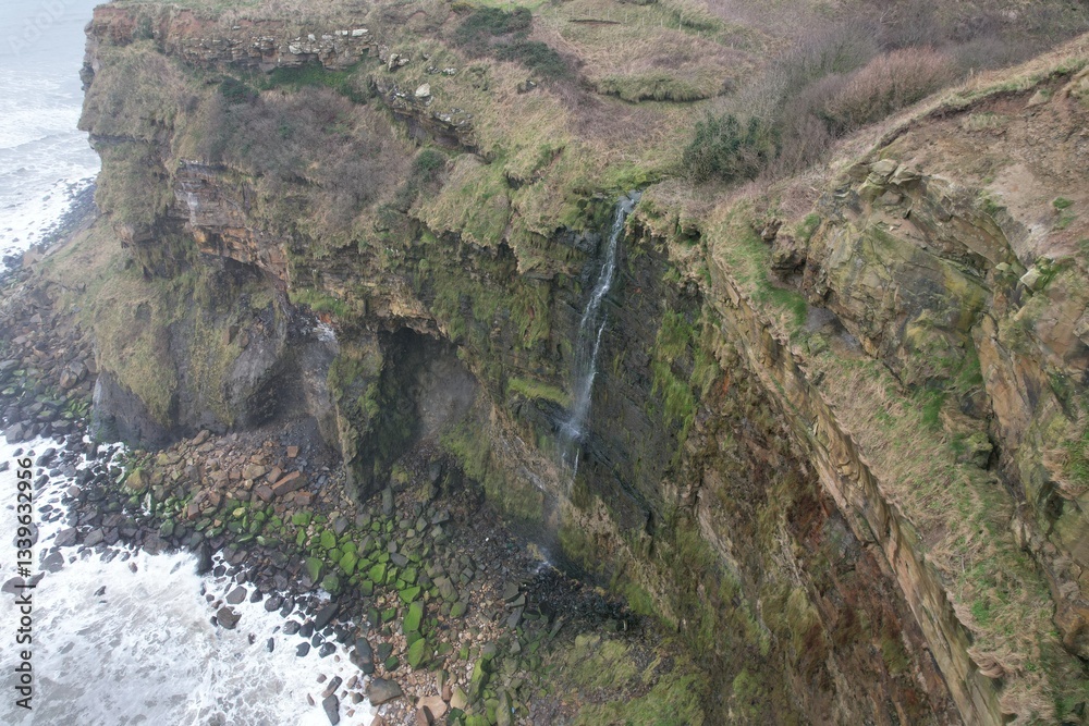 Obraz premium Coastal waterfall plunging into sea from cliffs between Scarborough and Whitby.