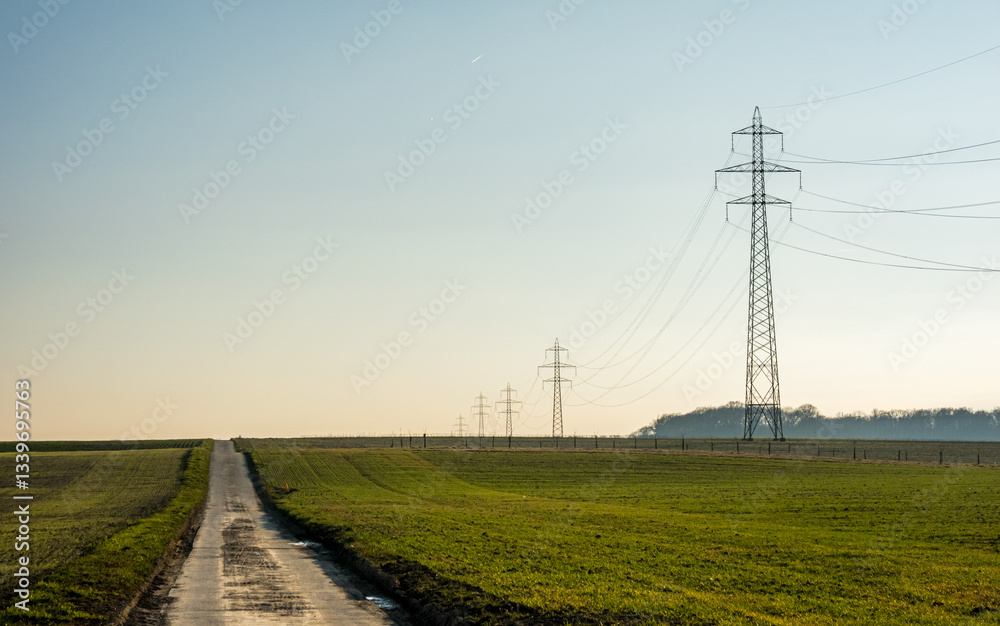 Rural road with transmission towers under clear blue sky Rural road with transmission towers under clear blue sky