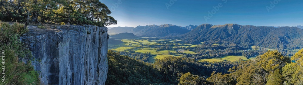 Breathtaking panoramic view of a lush green valley and majestic mountains from a high cliff in New Zealand.