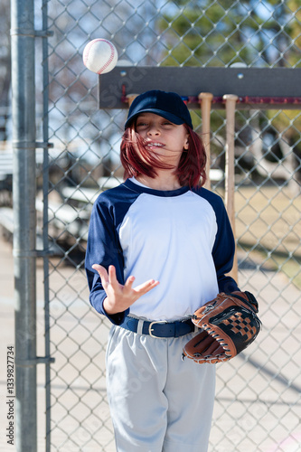 Young girl in little league baseball uniform with glove and ball in dugout