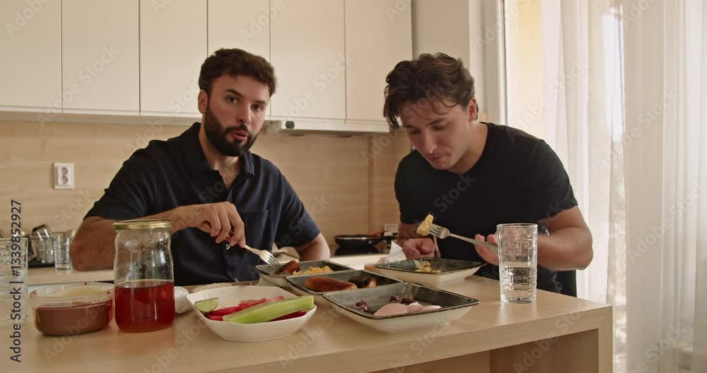 Two Caucasian men enjoy a healthy breakfast together in their modern kitchen. They share a meal and conversation, starting their day with positive energy.