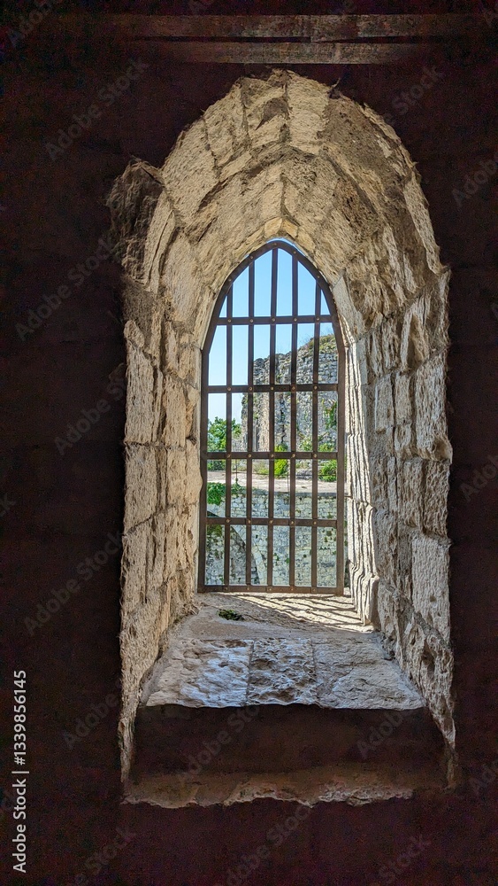 Fototapeta premium An exquisitely crafted stone window, elegantly framed with iron bars, presents a stunning picturesque view outside