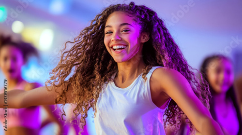 A smiling young woman with curly hair dances energetically in a brightly lit venue. Concept of joy and movement. For fitness or dance photo.