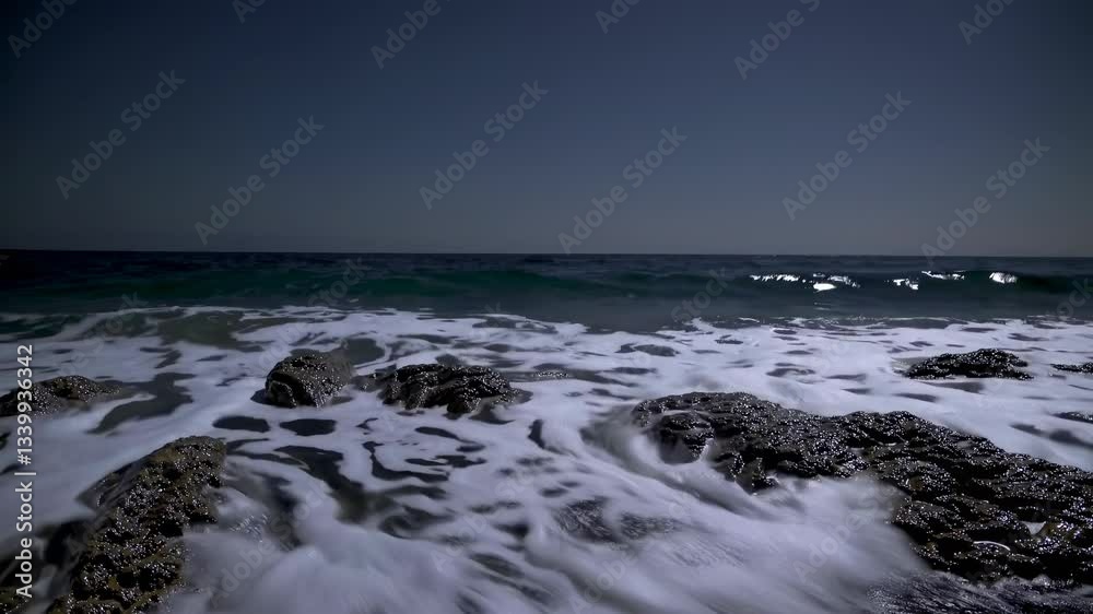 Powerful ocean waves crashing against rocky coastline during nighttime, moonlight illuminating dark seascape with dramatic, rhythmic water motion Powerful ocean waves crashing against rocky coastline during nighttime, moonlight illuminating dark seascape with dramatic, rhythmic water motion