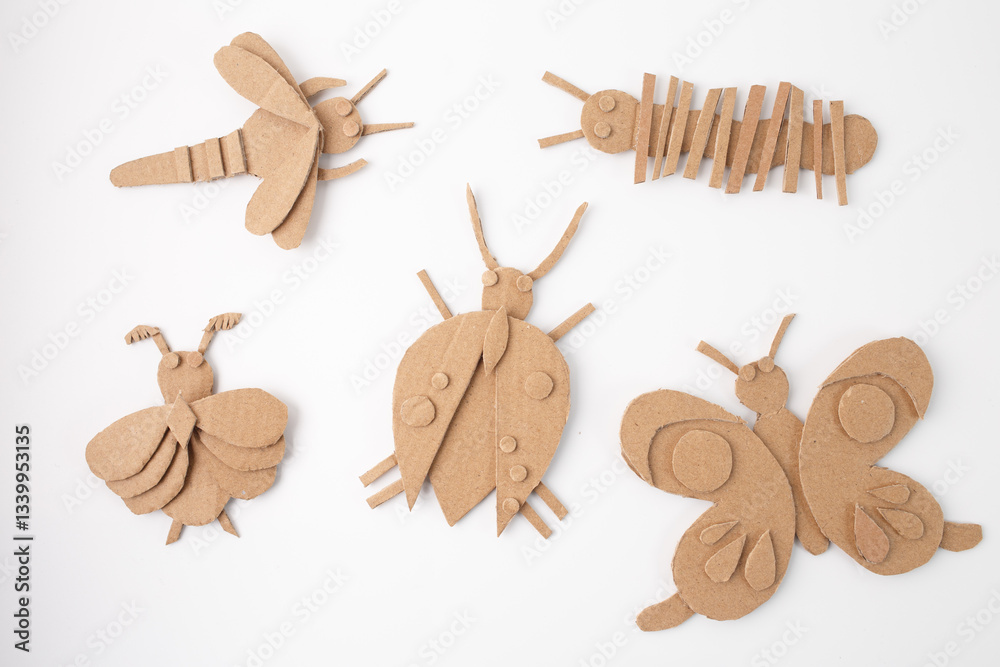 Fototapeta premium Handmade cardboard insect crafts arranged on white background. DIY eco-friendly bug figures including bee, butterfly, beetle, caterpillar, and moth. box craft for kids, toddler playtime,
