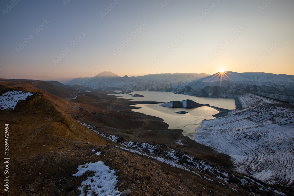 Obraz premium Sunrise above the Yeranos mountain range and Azat Reservoir during a cold winter morning, casting a golden glow over the snow-covered landscape. Great travel and photography destination