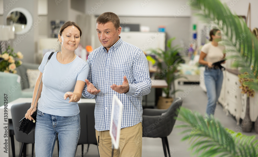 Happy married couple, adult man and woman choosing functional furniture for home in shop, discussing displayed samples Happy married couple, adult man and woman choosing functional furniture for home in shop, discussing displayed samples