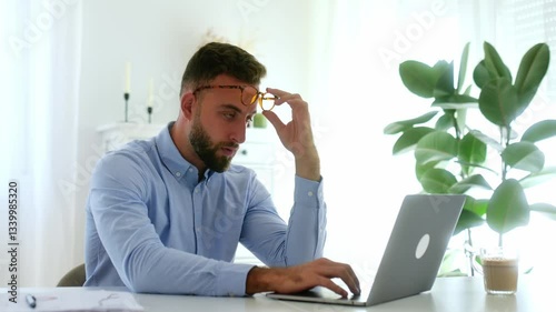 Exhausted sad businessman holds his hand to his bridgenose, reflecting on work challenges while working on his laptop, experiences stress and overwork, closed his eyes, need coffee break