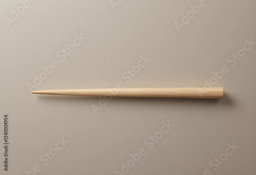 A single wooden chopstick rests diagonally on a smooth, neutral surface. Soft lighting highlights its texture and clean edges, creating a minimalist, balanced composition.
