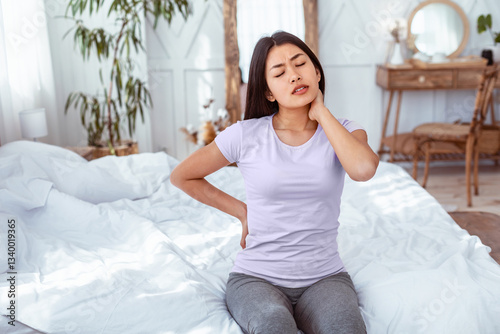 Arthritis Concept. Asian Woman Having Pain In Back And Neck Sitting In Bed At Home. Empty Space For Text