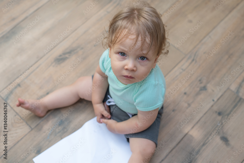 Naklejka premium Baby sitting on the floor holding a crayon near a blank paper
