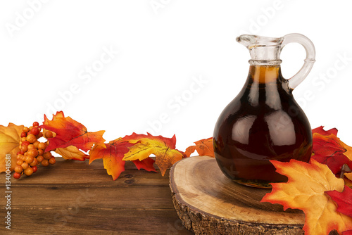 Obraz na płótnie Glass jug of maple syrup placed on a rustic wooden table with vibrant autumn leaves. A cozy and warm seasonal setting, perfect for fall-themed designs, food photography, and thanksgiving visuals. w salonie