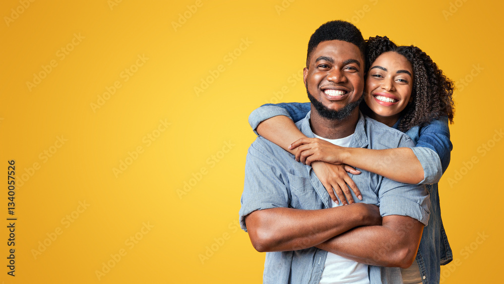 Fototapeta premium A joyful couple embraces playfully, showcasing their happiness with warm smiles. The bright yellow background enhances their cheerful connection in a sunny atmosphere.