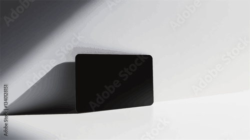 The image shows a black rectangular object, possibly a card or a tablet, positioned on a white surface.  The object is oriented horizontally.  A strong, diagonal shadow is cast on the surface from
