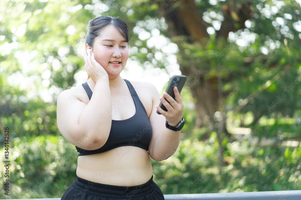 A plus size woman in activewear smiles while checking her phone outdoors, surrounded by greenery, promoting positivity and weight loss motivation. overweight asian woman A plus size woman in activewear smiles while checking her phone outdoors, surrounded by greenery, promoting positivity and weight loss motivation. overweight asian woman