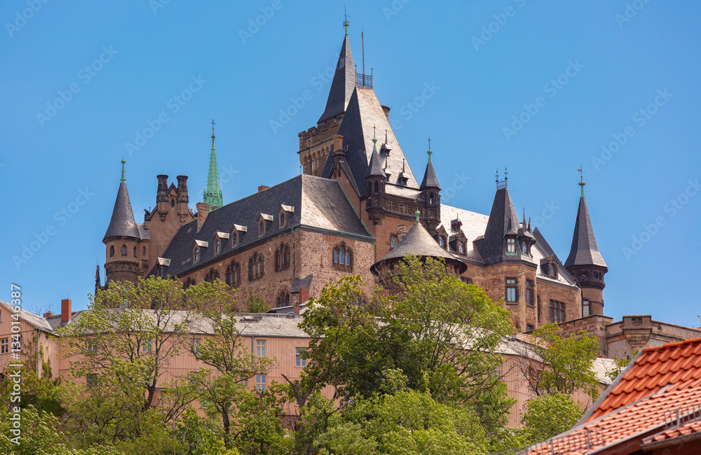 Fototapeta premium Wernigerode Castle, a historic hilltop castle with pointed towers and intricate architecture, surrounded by greenery in Wernigerode, Germany