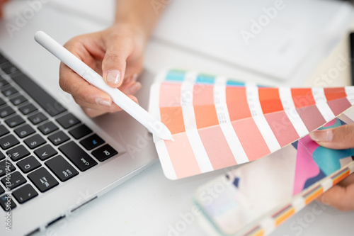 The hand holding a stylus pencil is choosing color from the printed color charts or color palettes.