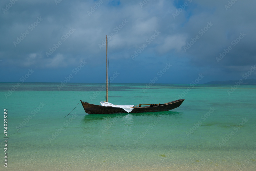 Fototapeta premium A small wooden fishing boat in the blue waters of the Pacific ocean on a cloudy day on the tropical Taketomi island in Okinawa Prefecture in Japan with space for text.