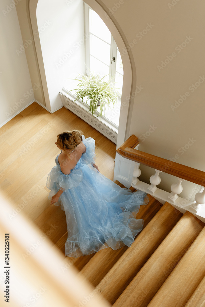 Fototapeta premium Young beautiful girl in blue dress of Regency era climbs wooden staircase. Classic artistic image of Russian literature of XIX century, outdated.