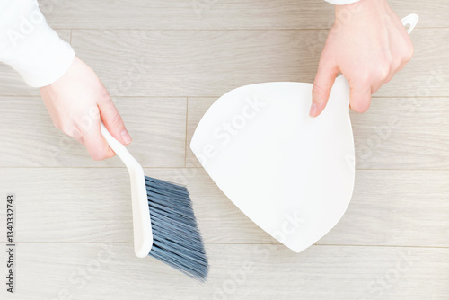 Female hands sweeping the floor with a brush and dustpan top view close-up.