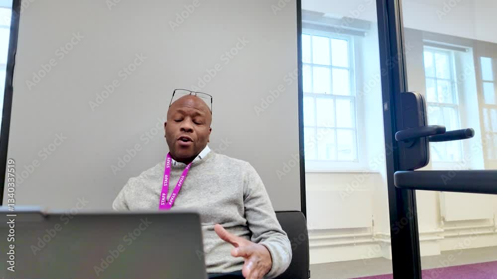 Black Businessman gesturing while talking in a modern soundproof office pod with a laptop on the desk Black Businessman gesturing while talking in a modern soundproof office pod with a laptop on the desk