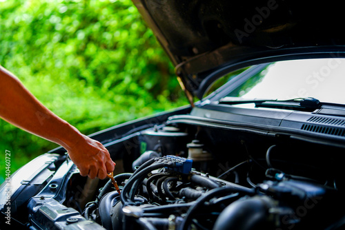 A mechanic holding an oil level gauge in one hand is checking the car's oil level for maintenance, Check  lubricant level at home, Close-up of details of the car engine compartment