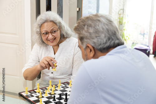 An elderly indian couple playing chess together at home. pastime, hobby, retirement life.