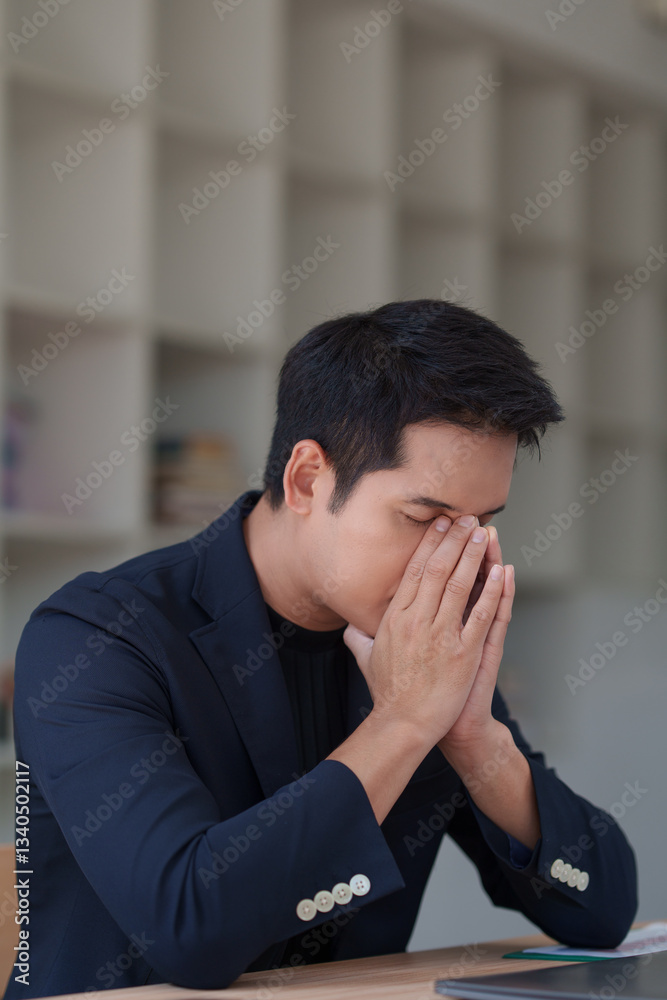 Young professional experiencing stress and frustration while working, covering his face with his hands at a desk in a modern office environment Young professional experiencing stress and frustration while working, covering his face with his hands at a desk in a modern office environment