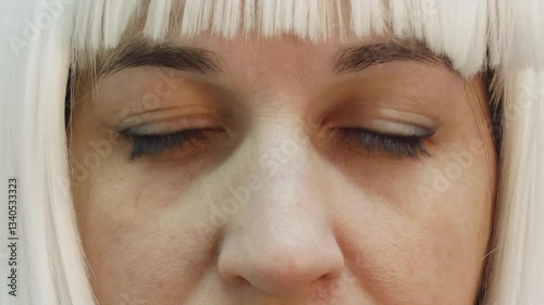 Close up capturing woman wearing white wig gradually opening brown eyes, revealing gradual transition between closed and open eye states with subtle facial expression and detail
