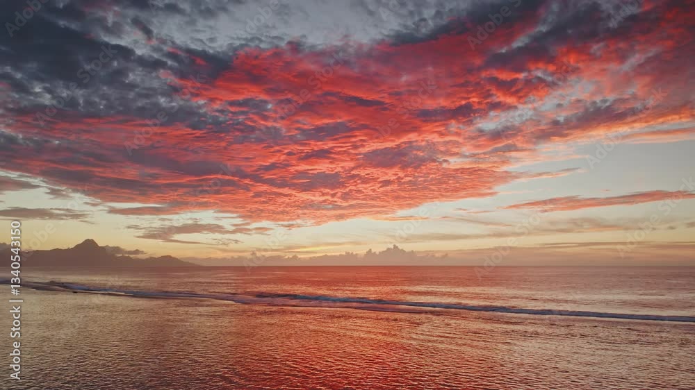 Breathtaking sunset over Tahiti island in French Polynesia, featuring vibrant red clouds reflecting on the calm ocean surface, creating a magical and serene atmosphere