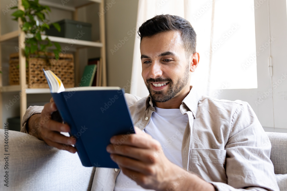 Caucasian adult man reading a book sitting on the sofa at home.