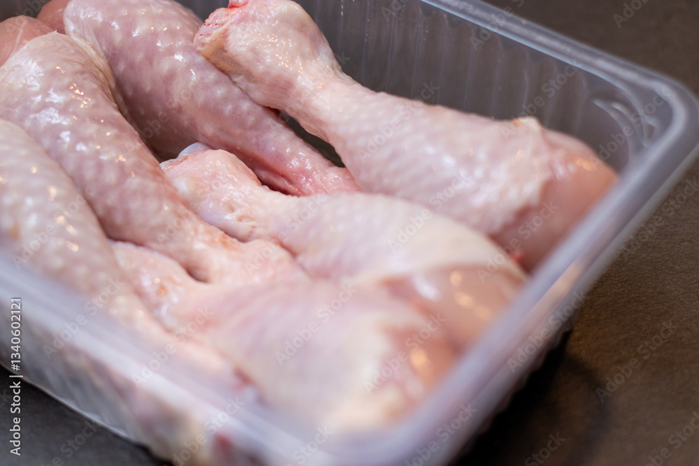 Close up of raw chicken drumstick in a plastic box on kitchen table Close up of raw chicken drumstick in a plastic box on kitchen table