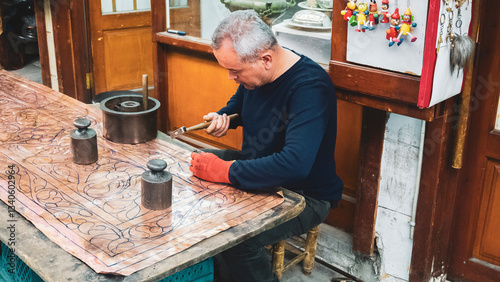 Copper craftsman shaping metal. Skilled artisan meticulously crafting intricate patterns on a copper sheet in a traditional workshop.
